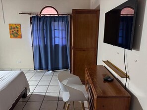 Une chambre d’hôtel comprenant un lit, un bureau avec une chaise, une télévision et une armoire en bois.