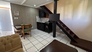 A living room with a sofa, a coffee table, a kitchen area with cabinets, a dining table, and a staircase. - Cozy Studio Apartment 2 min to the Beach, Rooftop (Sosúa)