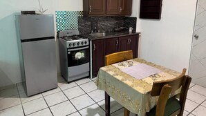 Cocina compacta con refrigerador, estufa y lavamanos, además de una mesa de comedor con una silla.