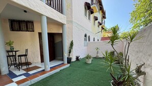 Un patio con césped artificial, plantas en macetas y un área de estar con sillas y una mesa.