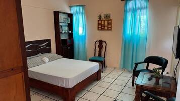 Un dormitorio con cama, escritorio, silla, estantería y televisor.