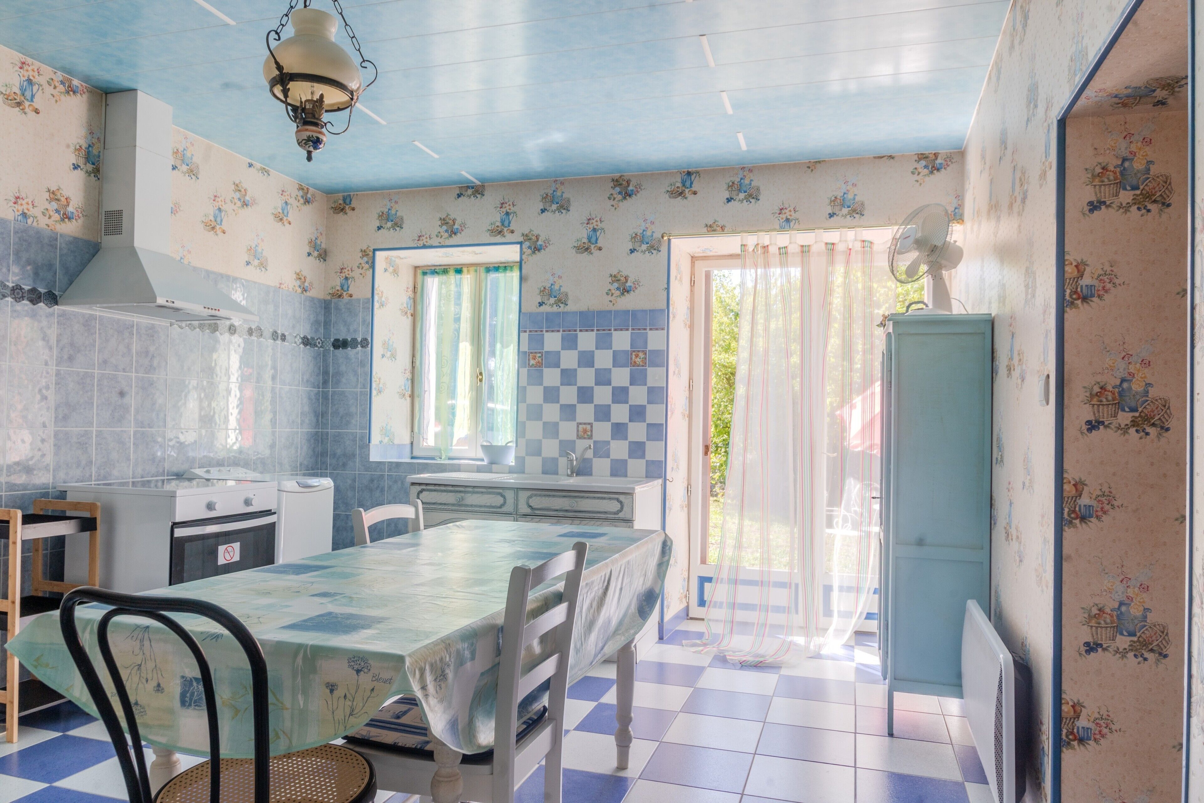 A kitchen with a checkered floor, a dining table, chairs, a stove, and a fan.
