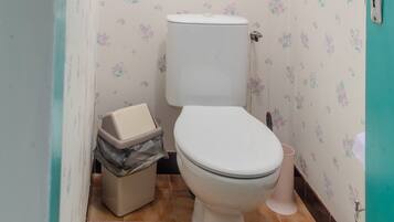Un baño con inodoro, un bote de basura y una pared con papel tapiz floral.