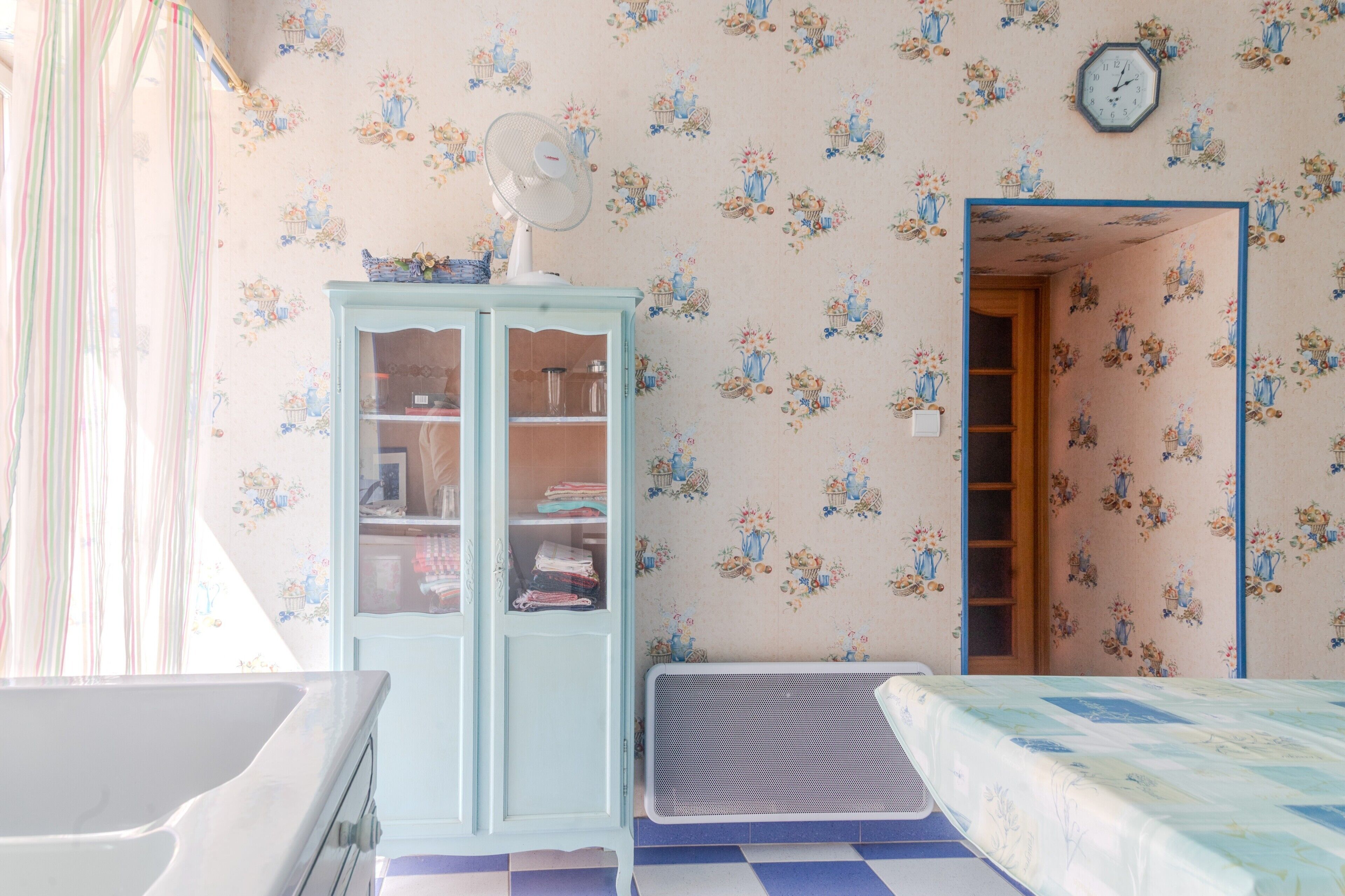 Una habitación con un armario azul, una cama, un radiador y un reloj en la pared.