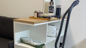 Un ambiente compatto con scaffalatura bianca integrata, un aspirapolvere e un divano scuro.
