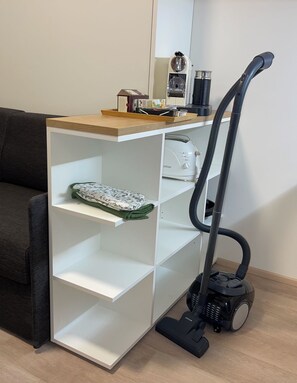 Un espacio habitable pequeño con un mueble blanco empotrado, un aspirador y un sofá de color oscuro.