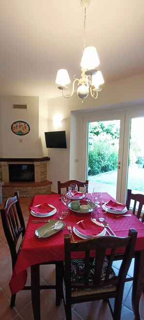 A dining area with a red tablecloth, wooden chairs, and a fireplace.