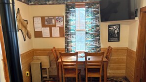 A cozy room with a wood-burning stove, a dining table with chairs, a patterned rug, and a bulletin board with notices. - Great cabin to stay on fishing trip or ATV/UTV trip. (Hayward)