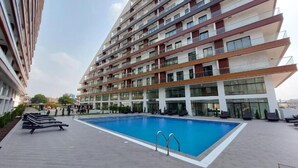 A modern apartment building with a rooftop swimming pool, multiple balconies, and a landscaped terrace.