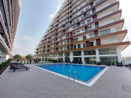 A modern apartment building with a rooftop swimming pool, multiple balconies, and a landscaped terrace.