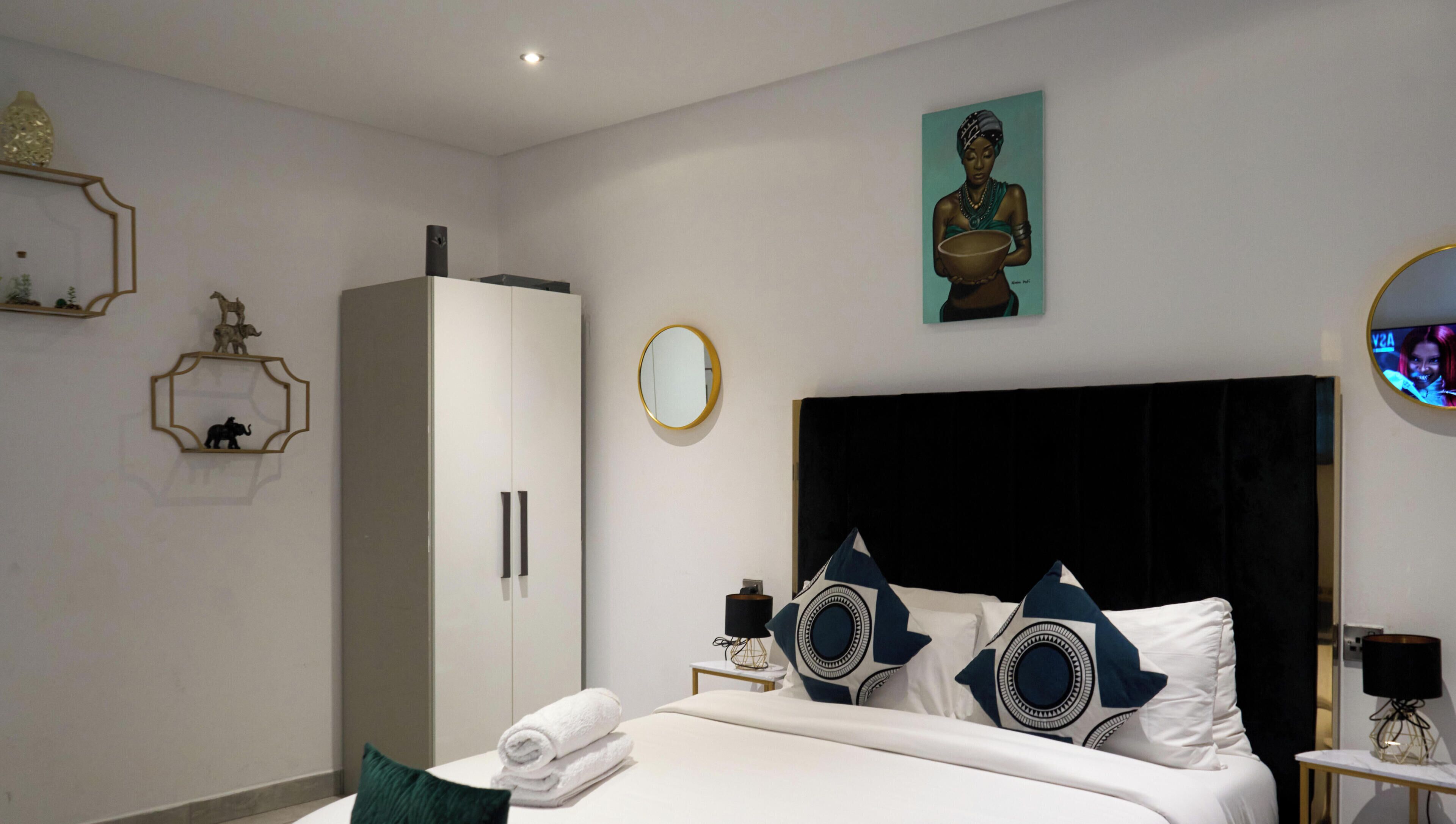 Une chambre d’hôtel moderne avec un grand lit, une armoire, un miroir rond et un tableau au mur.