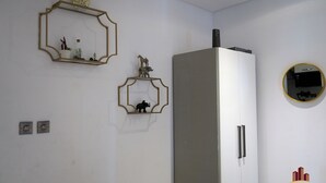 A kitchen with a white refrigerator, two wall-mounted light switches, and decorative wall art including a framed mirror and two animal figurines.