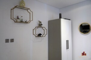 A kitchen with a white refrigerator, two wall-mounted light switches, and decorative wall art including a framed mirror and two animal figurines.