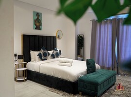 A modern bedroom with a large bed, a bedside table, a mirror, and a green ottoman.