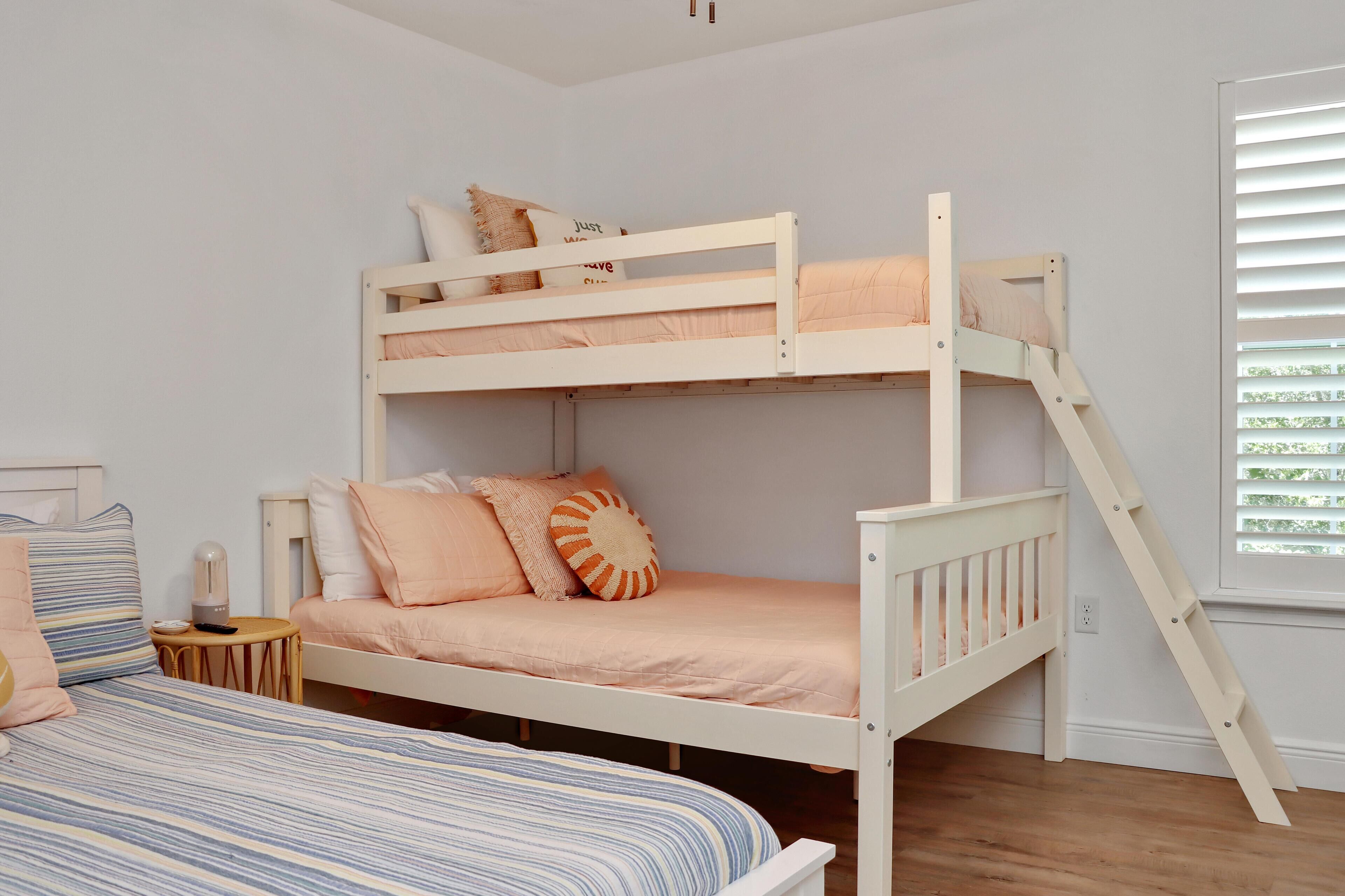 A bunk bed with two levels, a small bedside table with a lamp, and a window with blinds.