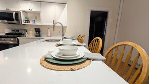 Cocina moderna con armarios blancos, electrodomésticos de acero inoxidable y una isla grande con lavaplatos y zona de comedor.