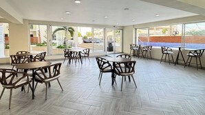 Un espace intérieur vaste et lumineux, avec de nombreuses tables et chaises, de grandes fenêtres et un sol décoré de motifs en chevrons.