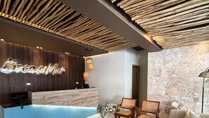 Un espace d’accueil doté d’un plafond en bois, d’un comptoir de réception avec un dessus en marbre et d’un coin salon avec un canapé et des fauteuils.