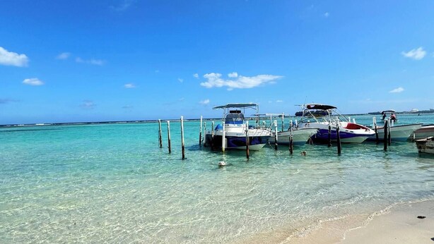 Une plage à l’eau turquoise et limpide, où des bateaux sont amarrés le long du rivage.