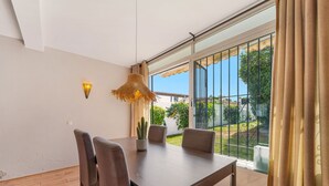 Un espace repas comprenant une table, des chaises, un luminaire suspendu et une vue sur l’extérieur.