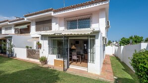 Un bâtiment blanc avec un toit en tuiles, une terrasse avec une table et des chaises, et une cour clôturée.