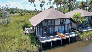 A two-story house with a balcony, surrounded by water and vegetation.