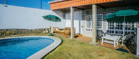 Un patio trasero con piscina, muros de piedra y mobiliario exterior.