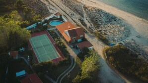 An aerial view of a coastal property with a swimming pool, tennis court, and beachfront access.