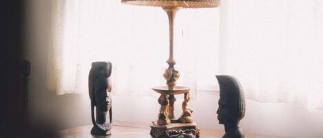 A table with a lamp and two sculptures in a dimly lit room with a window in the background.