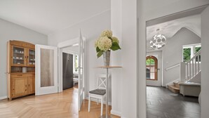 A spacious hallway with a wooden cabinet, a white chair, and a tall vase with flowers. - 19 min to the center - 250 m² / 2,691 sq ft - top villa from 1923 - 4BR 3,5BA (Gräfelfing)