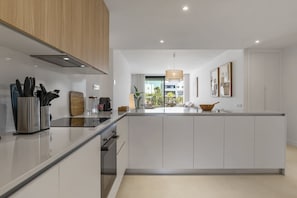 A modern kitchen with white cabinetry, a central island, and a view of the outdoors. - Lani | Terrace - pool - garden (Estepona)