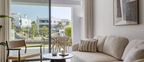 A modern living room with a sofa, a chair, a round table, and a view of a balcony with outdoor furniture.