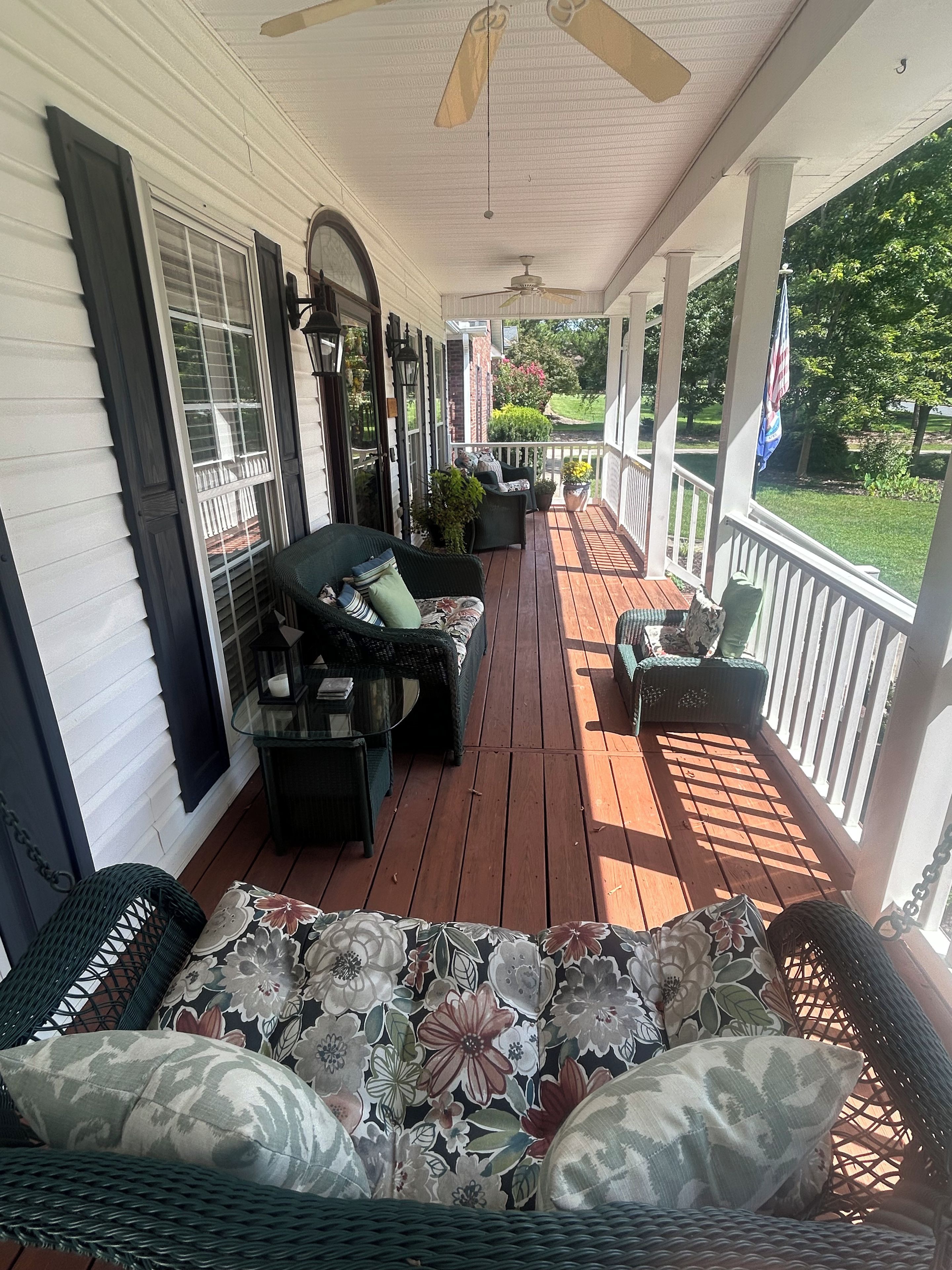 A covered porch with outdoor furniture, a ceiling fan, and a view of a garden.