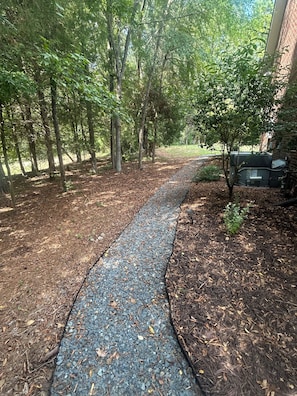 A paved pathway surrounded by trees and mulch, leading to a building with a brick exterior.