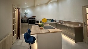 Een moderne keuken met een centraal eiland, een eethoek met een blauwe stoel, en een keukenblad.