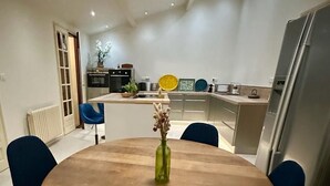 Een moderne keuken met een centraal eiland, een eettafel met stoelen en een koelkast.