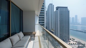 Varanda com sofá e mesa, com vista para a praia e edifícios altos.