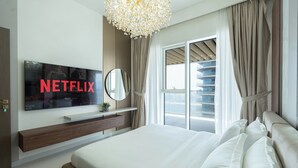 Quarto de hotel moderno com uma cama grande, televisão na parede, mesa de cabeceira e vista para a cidade pela janela.