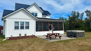A white house with a large porch, a hot tub, and a picnic table.