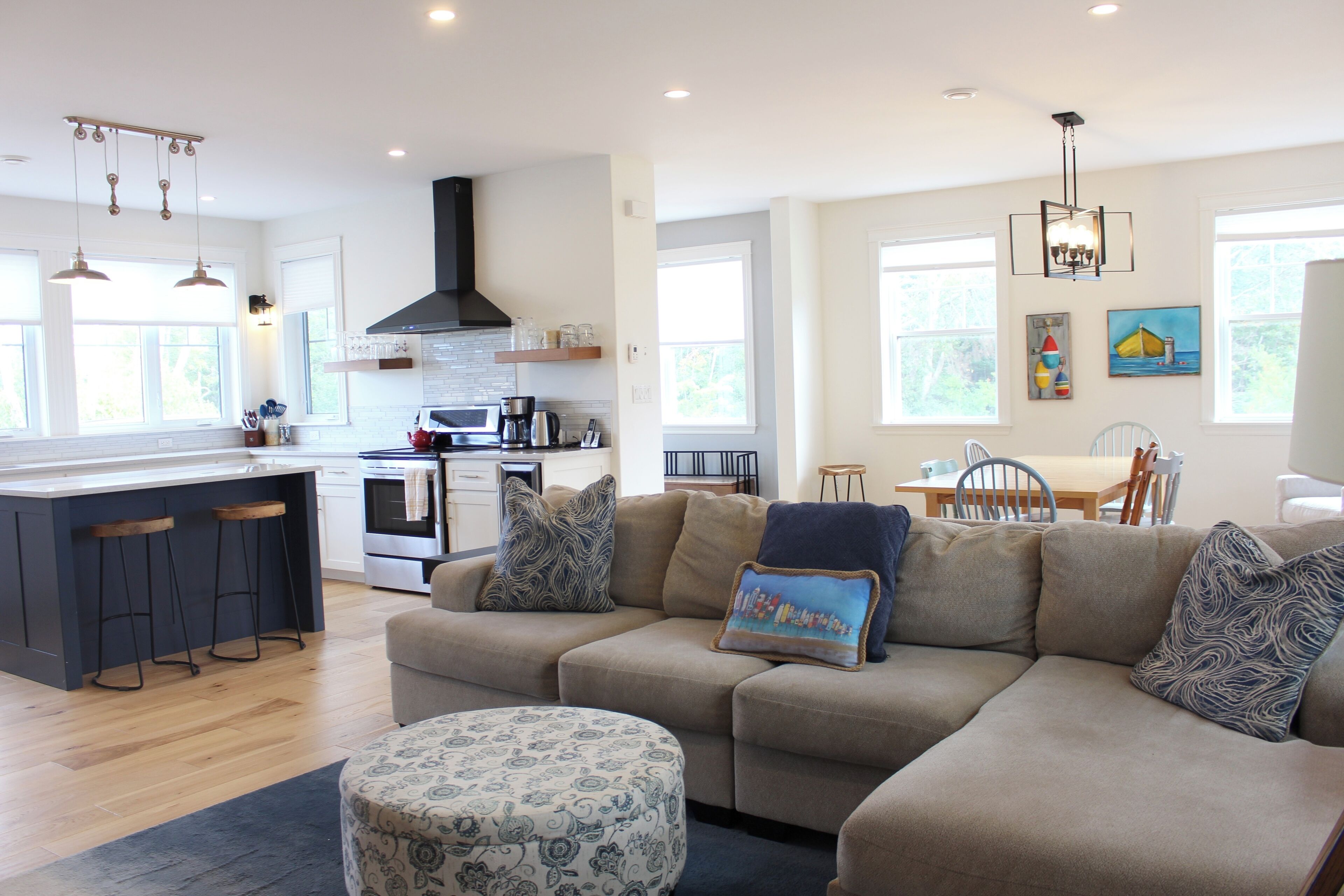 Een moderne keuken met een centraal eiland, een eethoek met een tafel en stoelen, en een woonkamer met een bank en voetenbank.