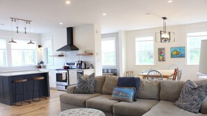 A modern kitchen with a central island, a dining area with a table and chairs, and a living room with a sofa and ottoman.