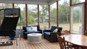 A covered outdoor area with a basketball hoop, two sofas, a round coffee table, and a wooden dining table.
