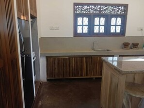 Une cuisine compacte dotée d’un réfrigérateur encastré, d’un évier et d’une fenêtre ornée d’un treillis décoratif.
