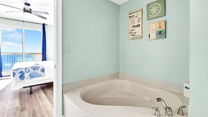 Une salle de bain avec une grande baignoire, un ventilateur de plafond et une vue sur le balcon.