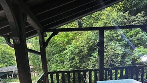 A covered outdoor area with a wooden deck, a table with chairs, and a view of a green forest. - Terrific villa with AC in charming Sarajevo (Sarajevo)