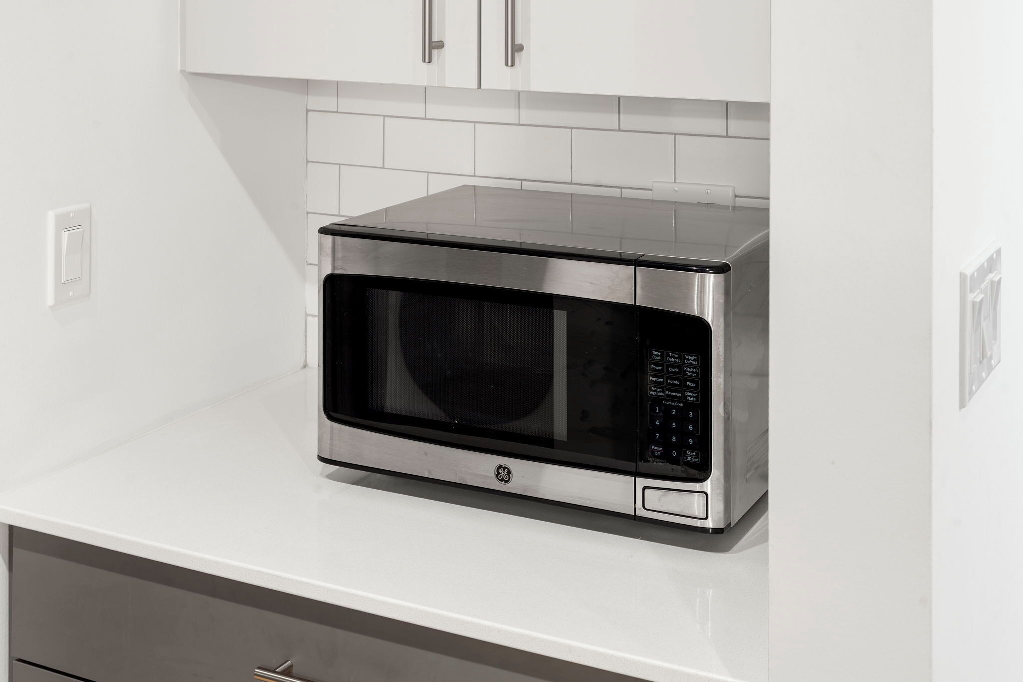 A GE microwave oven on a white countertop with a tiled backsplash.