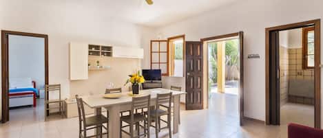 A spacious living area with a dining table, chairs, a ceiling fan, and a kitchen area.