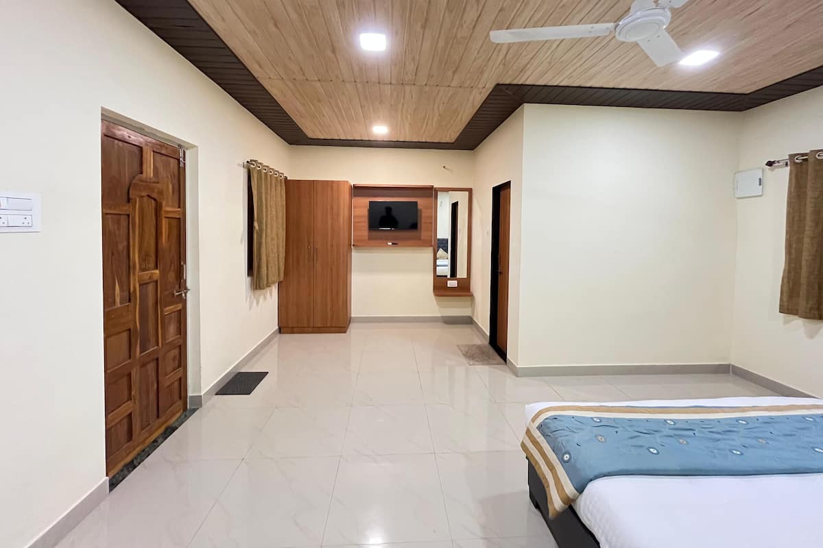 A hotel room with a bed, a ceiling fan, a TV mounted on the wall, and a wooden wardrobe.