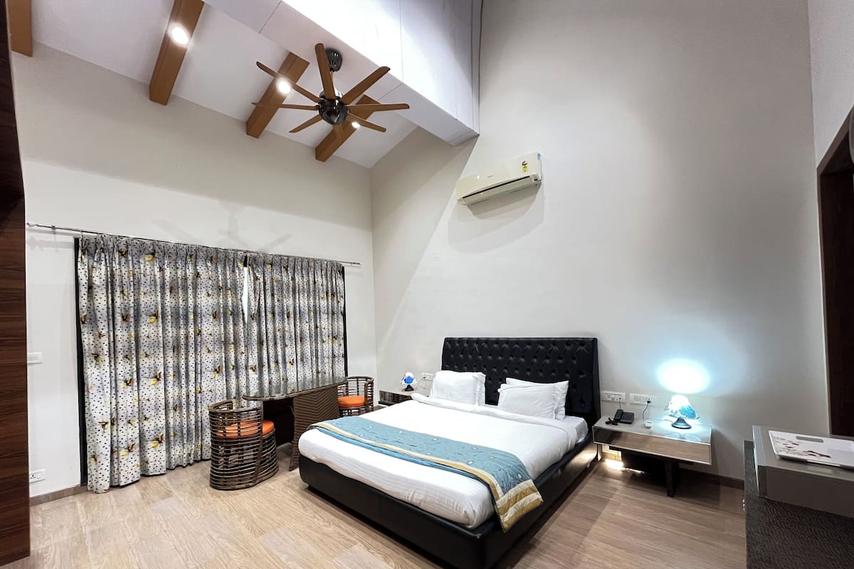 A modern bedroom with a large bed, a ceiling fan, an air conditioning unit, and a bedside lamp.