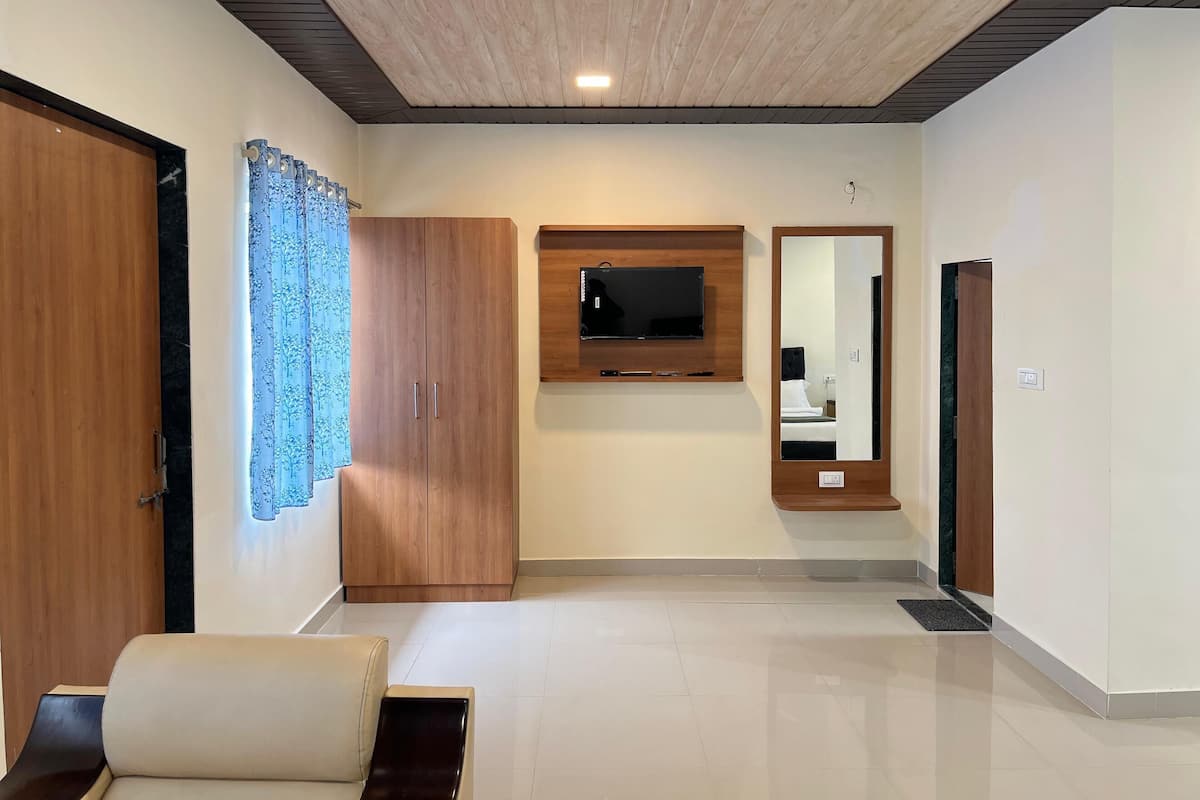A hotel hallway with a wooden wardrobe, a mounted TV, a mirror, and a seating area.